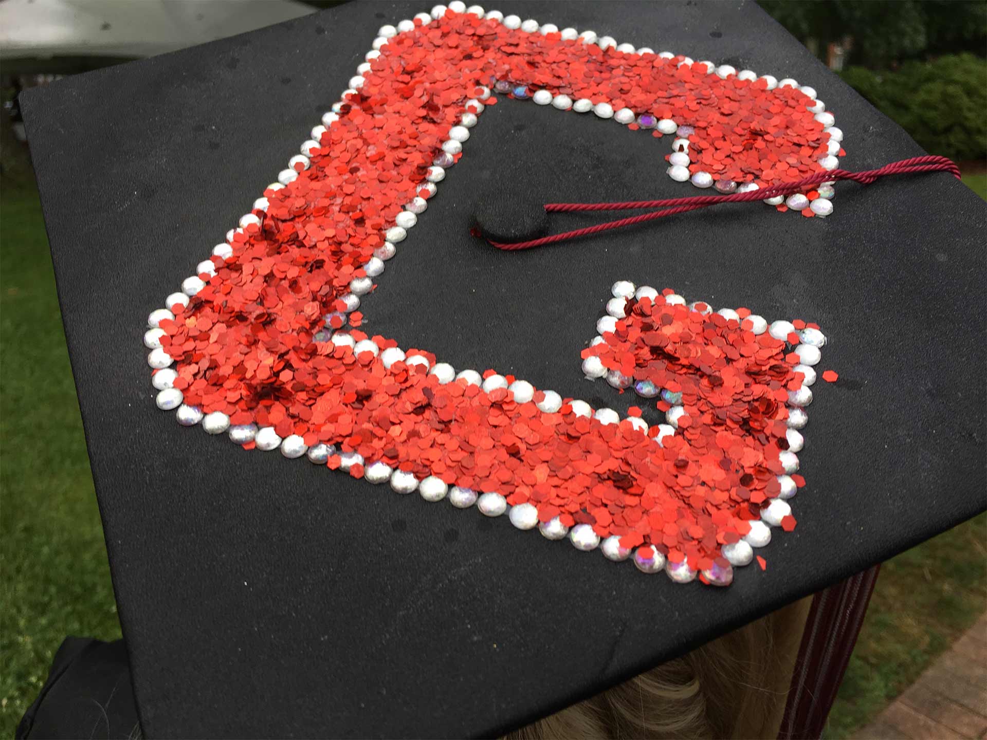 A student's mortarboard is decorated with a sparkly red G for Guilford.