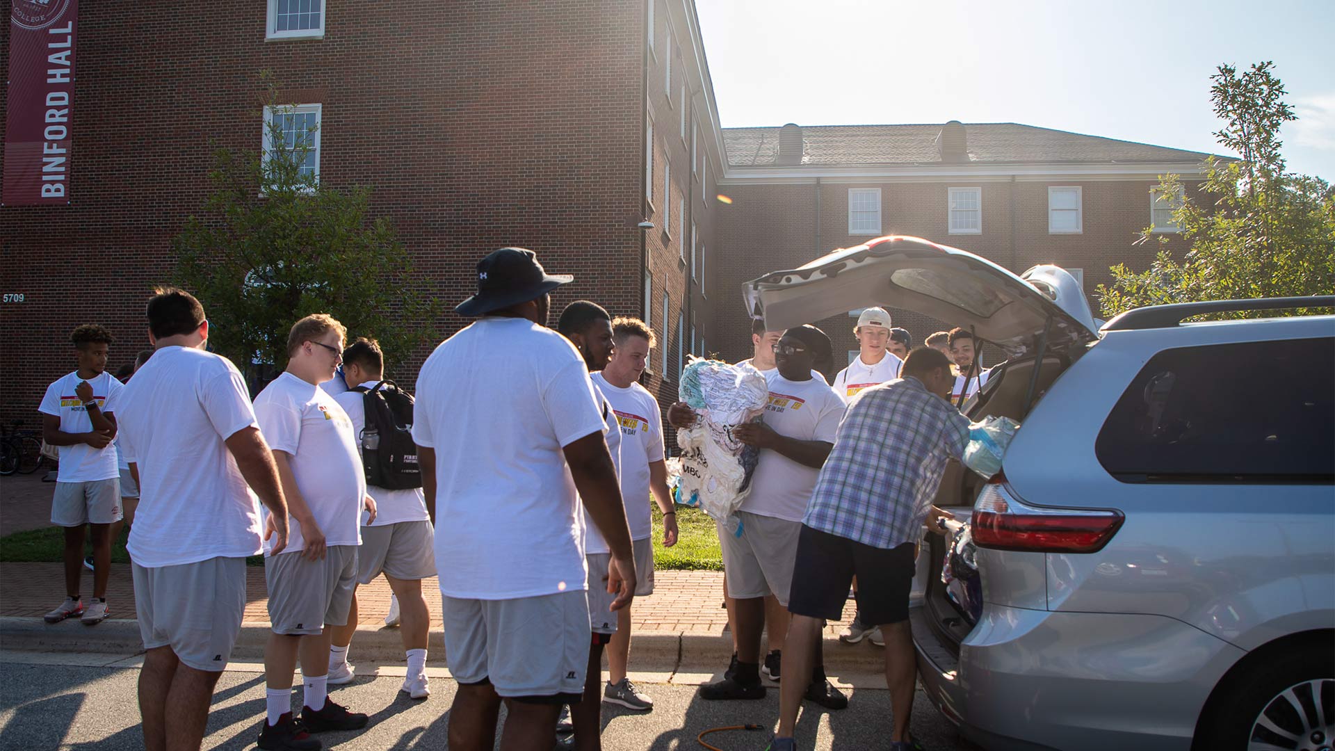 Members of the College football team unload a new student's car at Binford Hall.