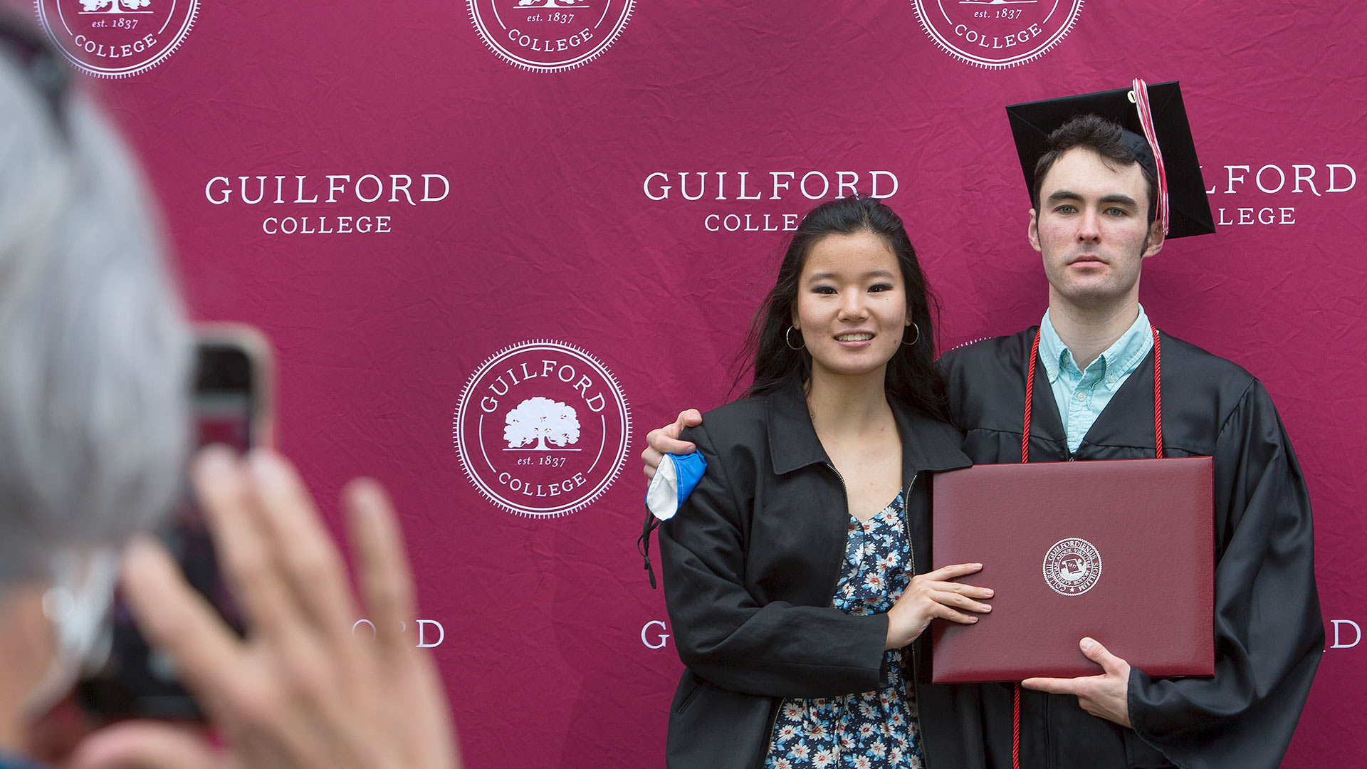 A graduate takes a photo with a friend.