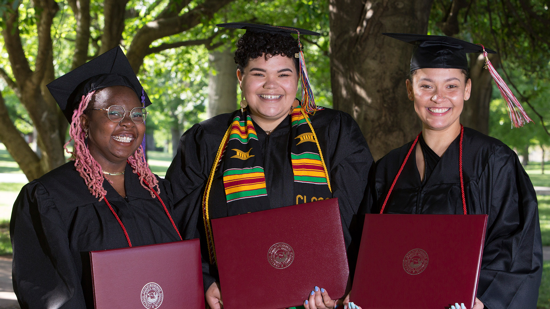 Three graduates stand together outside Dana Auditorium.