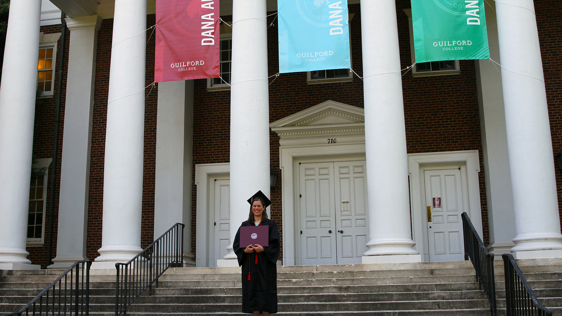 A student holds their diploma on the steps in front of Dana Auditorium.