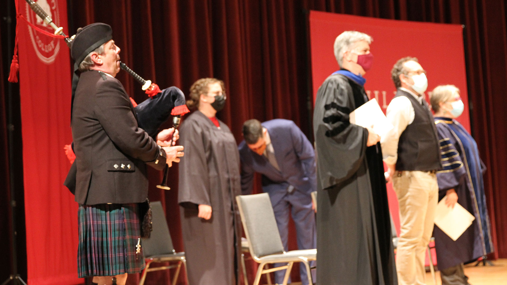 The traditional bagpiper plays on stage, standing beside the Convocation speakers.