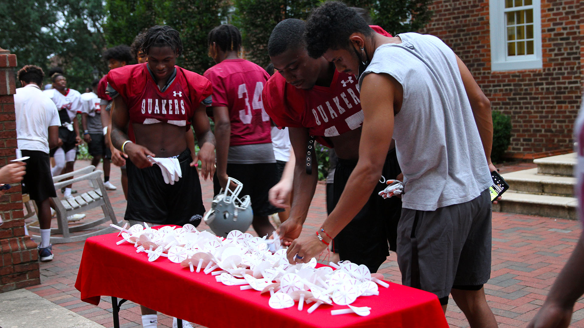 A group of football players wearing their red Guilford jerseys select white candles from the table before the Passing of the Light.