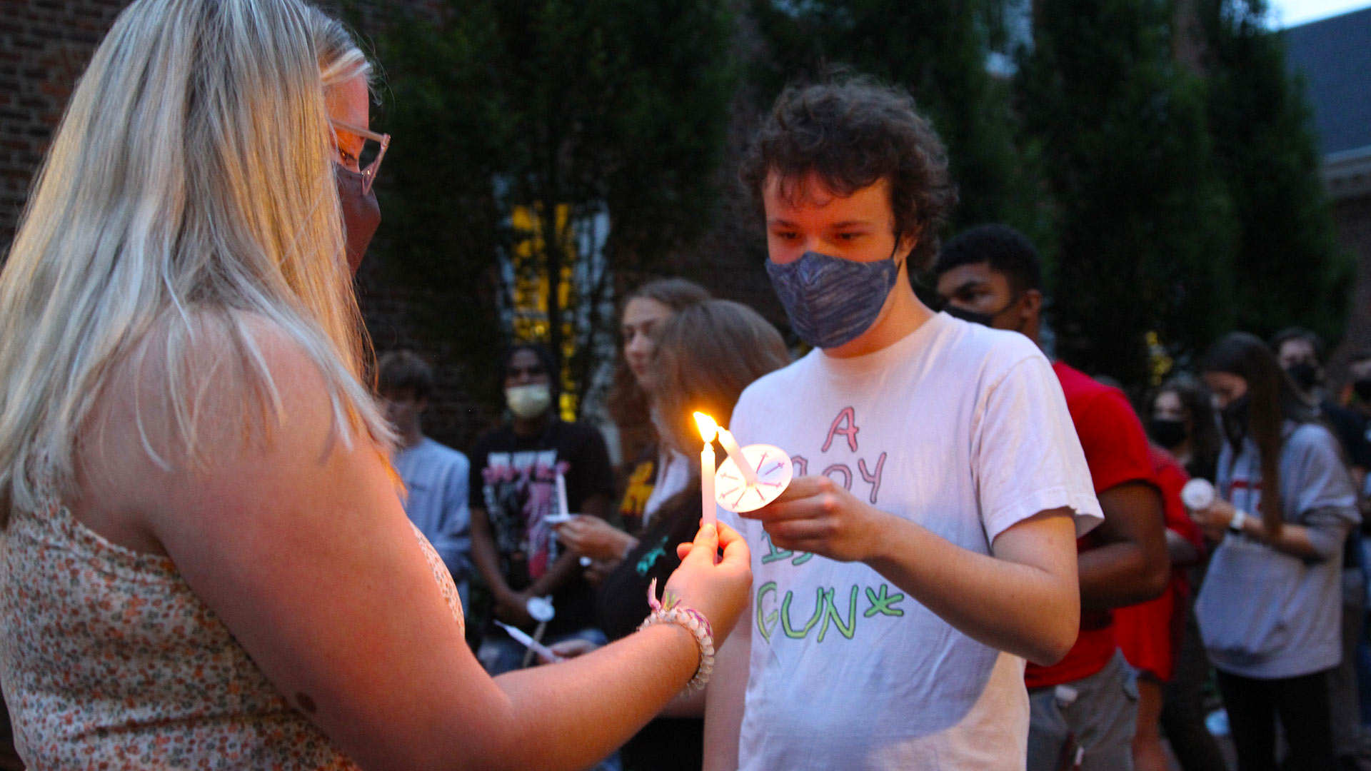 A masked student lights the candle of a student next to them.