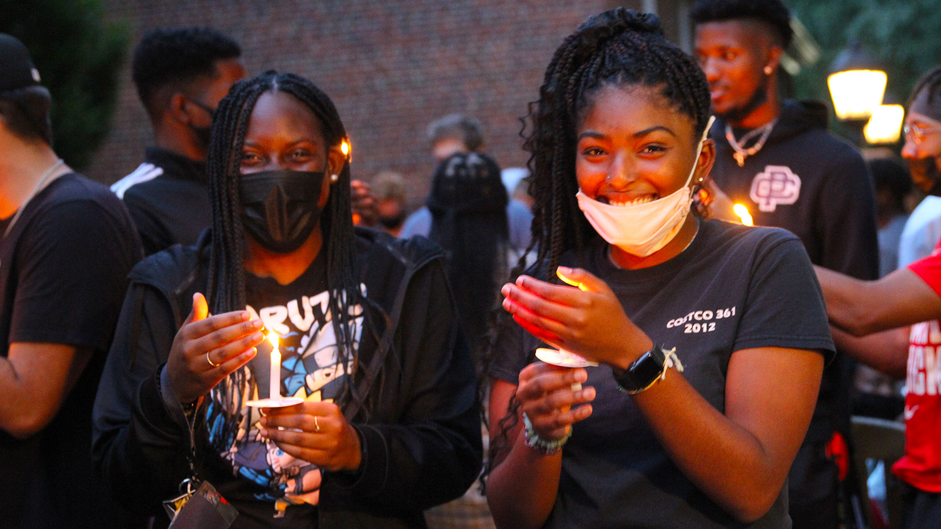 Two students protect their candle flames while they smile at the camera.