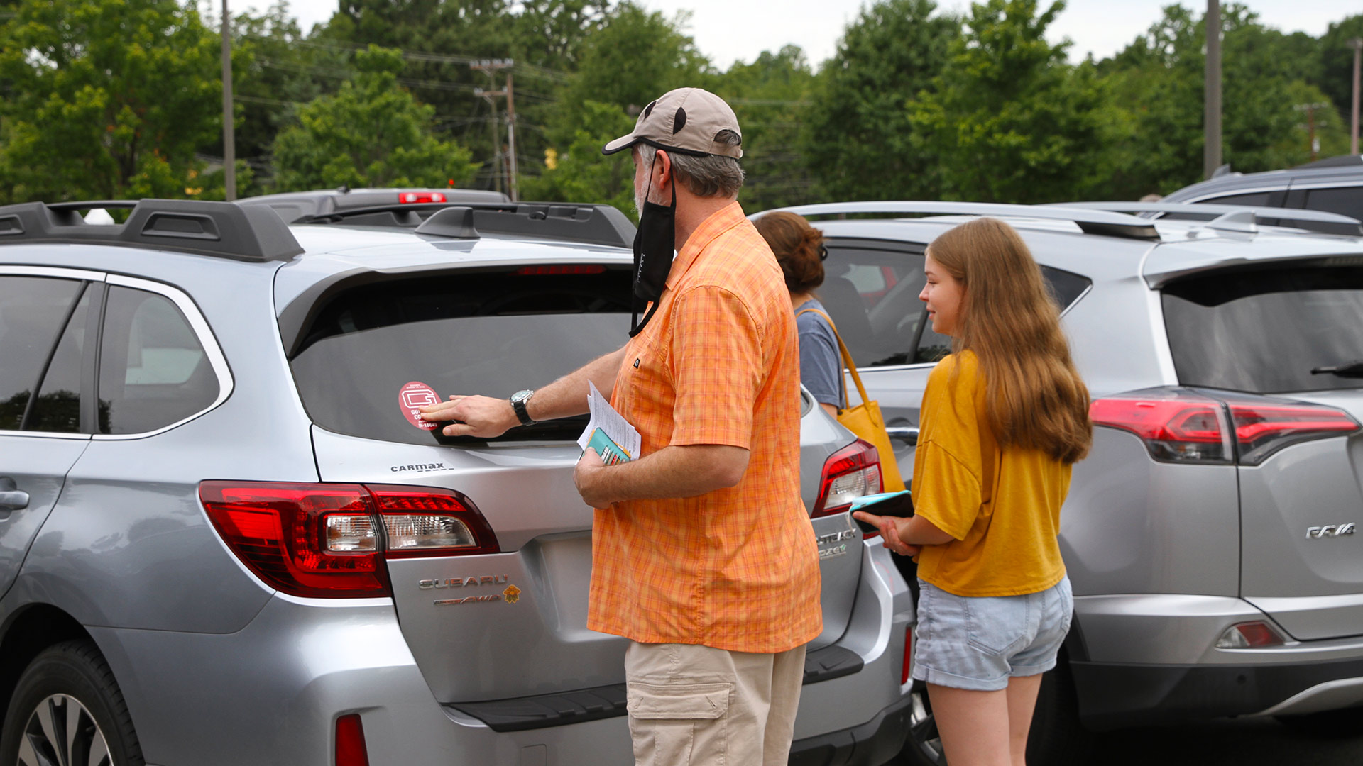 A parent applies a new Guilford parking sticker to the back of a student's car.