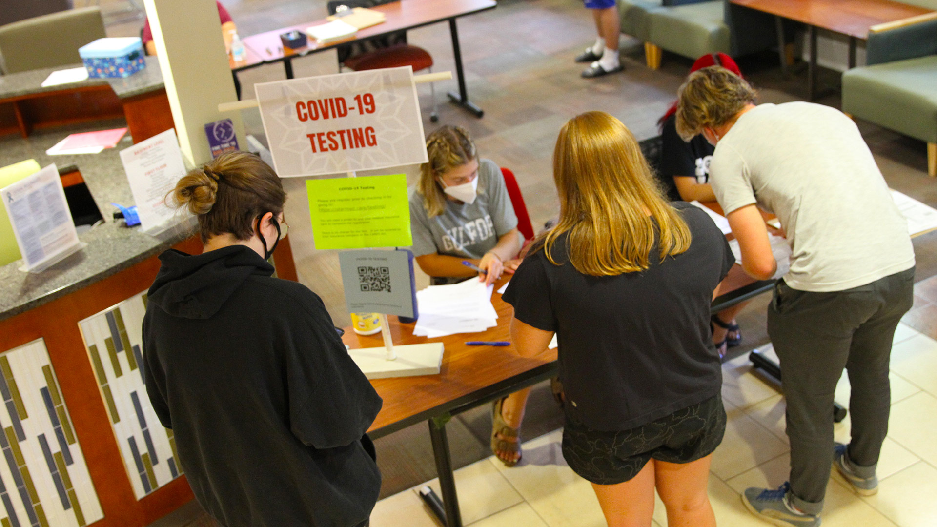 Three students stand in line at the COVID-19 Testing sign-up table.