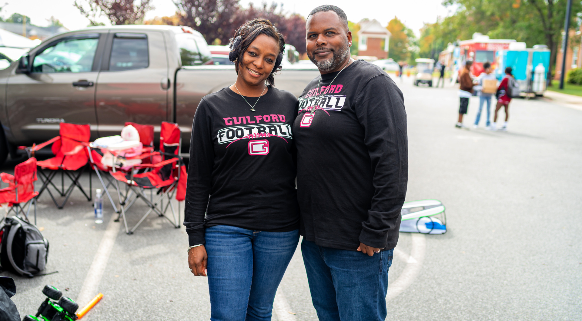 Two Guilfordians wearing black Guilford Football shirts pose for a photo during tailgating.