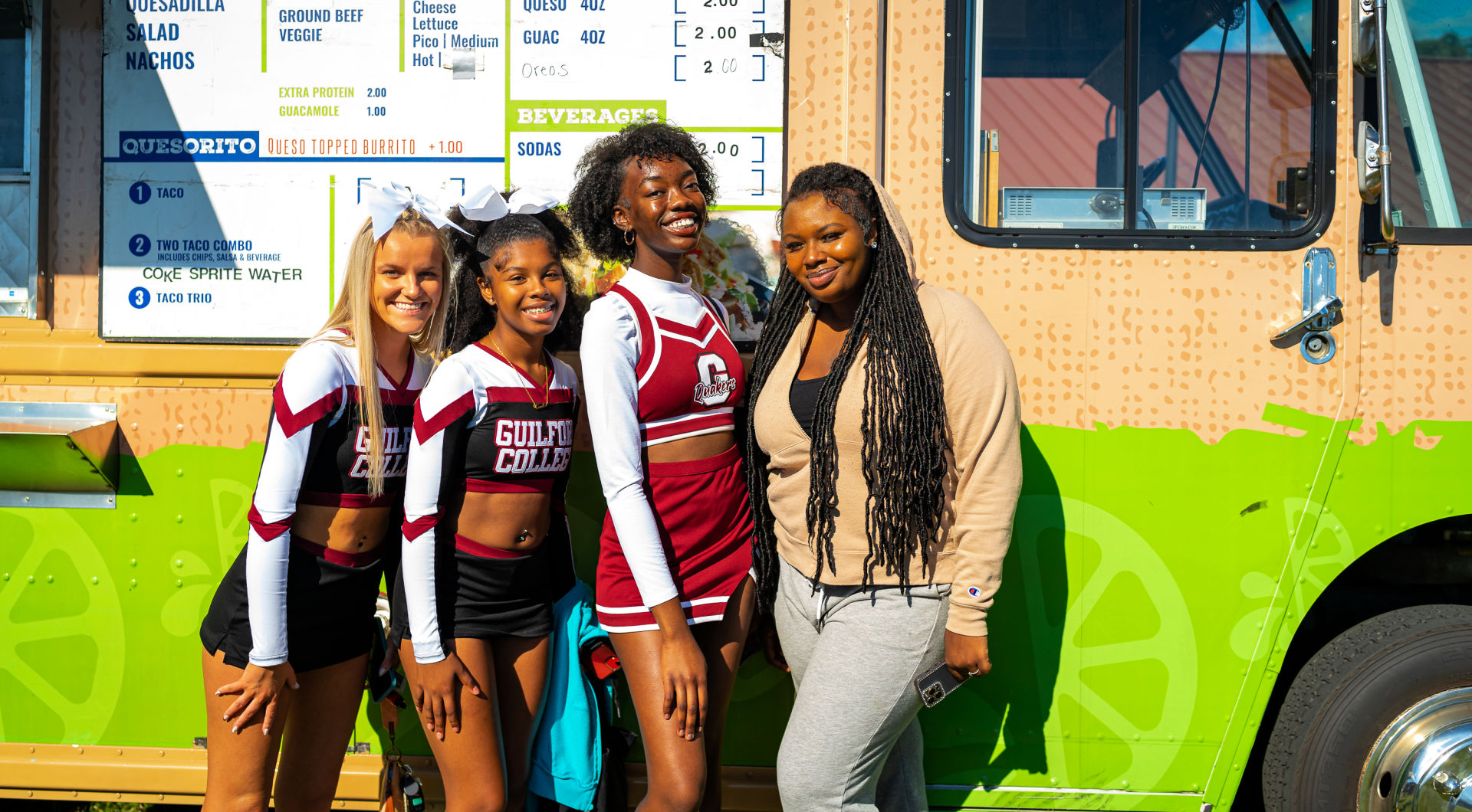 Three Guilford cheerleaders and a friend take a photo beside a food truck.