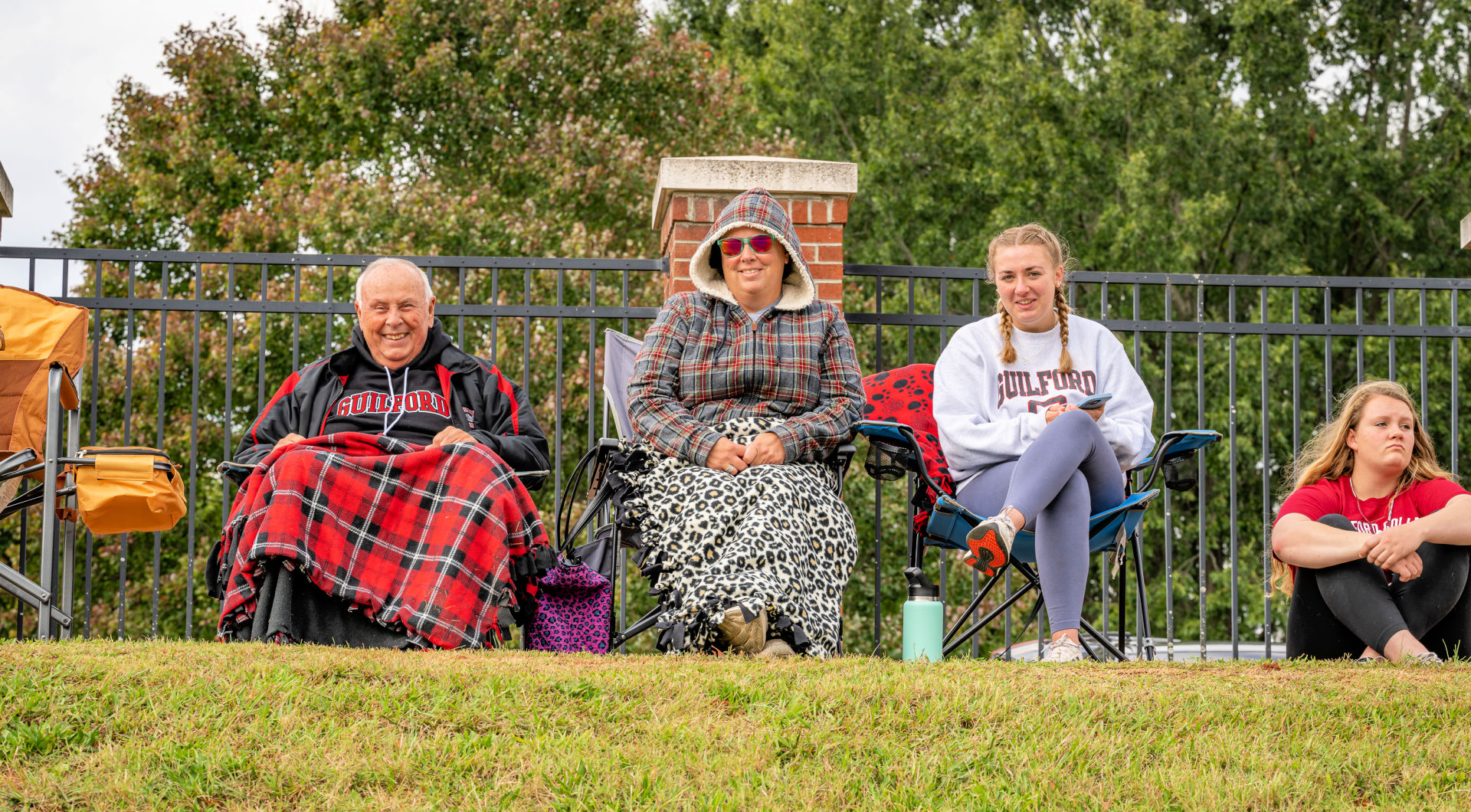 Three Guilfordians, two under blankets, watch a game from the hill.