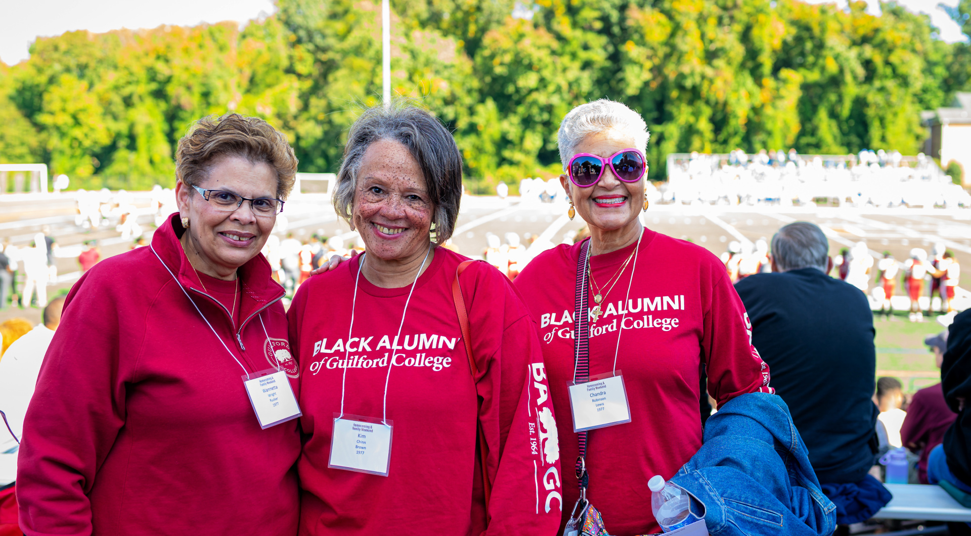 Three Black alumni of Guilford take a group photo in front of the football field.