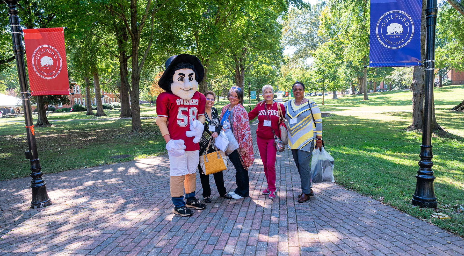 The Quaker Man takes a photo with three Guilfordians on the Quad.