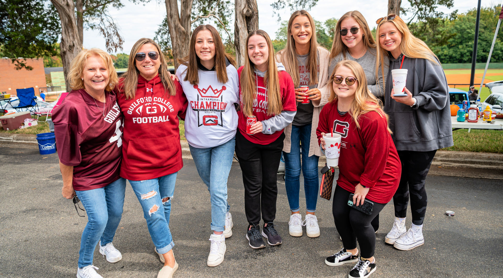 A group of eight Guilfordians wearing Guilford shirts takes a photo while tailgating.