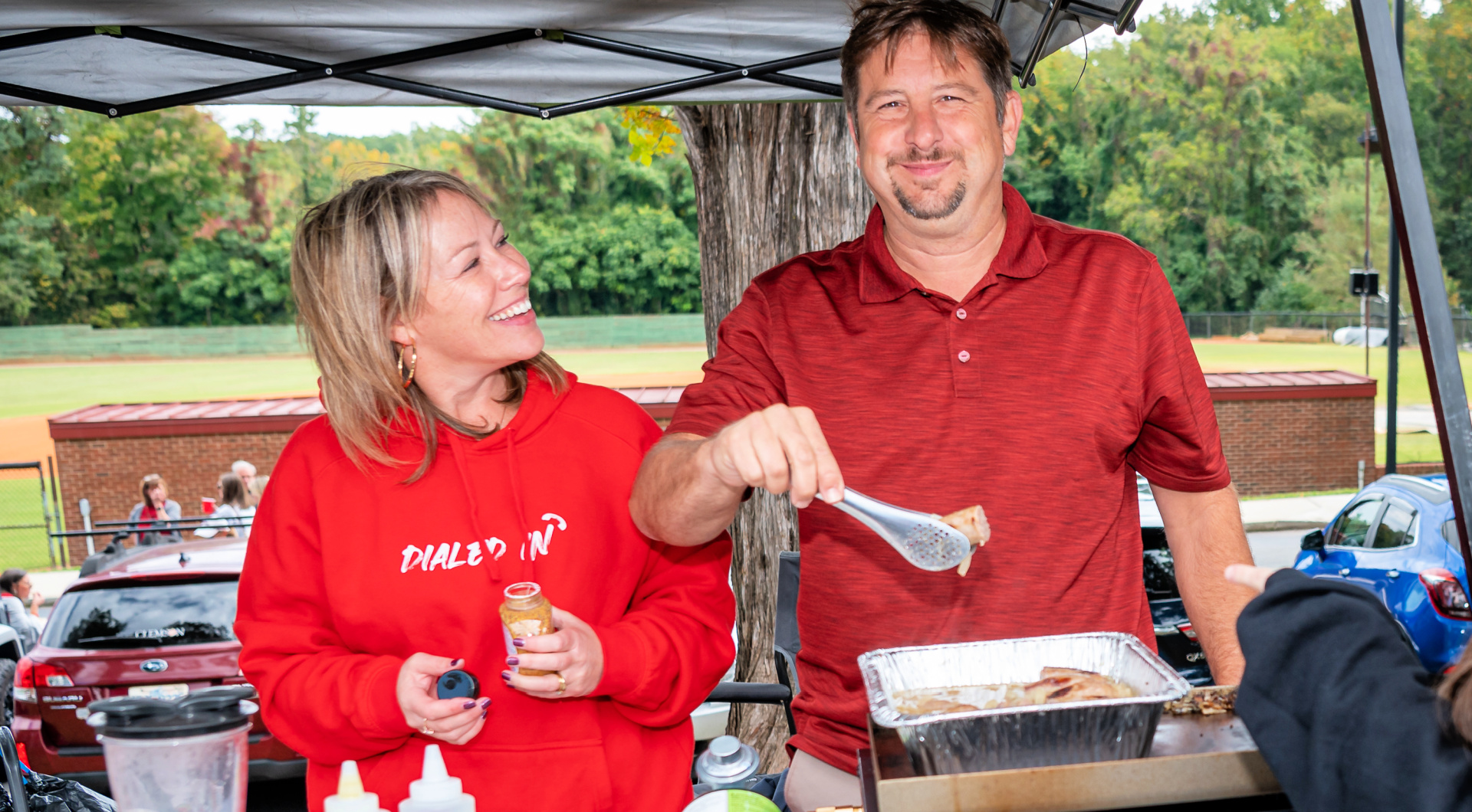 Two Guilfordians smile while serving lunch at their tailgate.