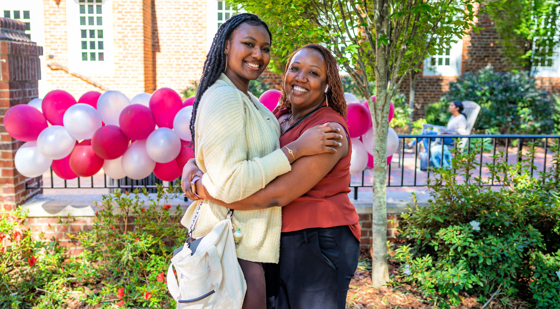 Two Guilfordians hug in front of balloons during Homecoming festivities.