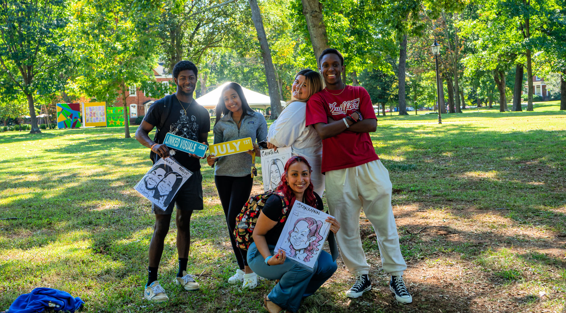 Five students take a photo with art work they made at Homecoming.