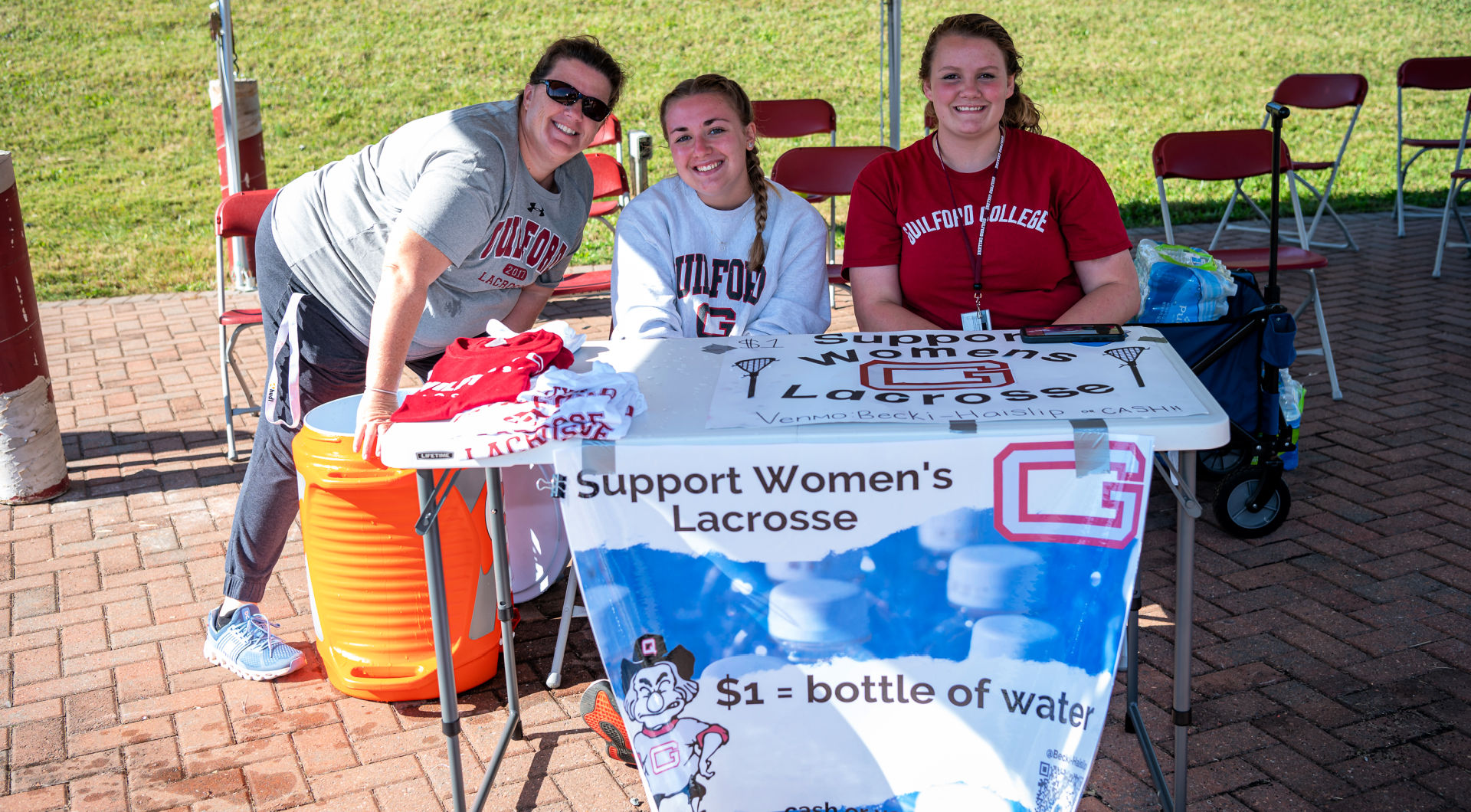 Members of the women's lacrosse team sit at a table selling water and raising money for their team at Homecoming.