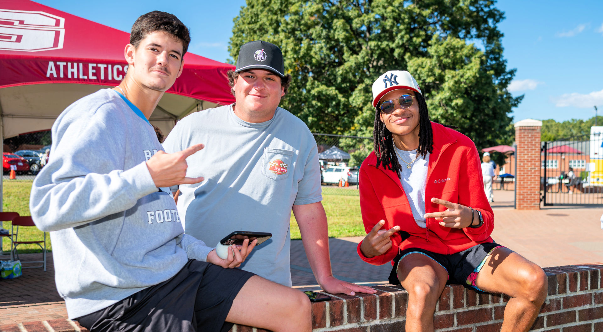 Three Guilfordians sit on a wall in the football stadium.