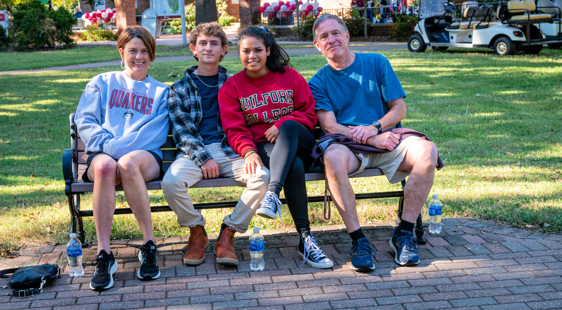 Four Guilfordians, two wearing Guilford sweatshirts, sit on a bench on the Quad.