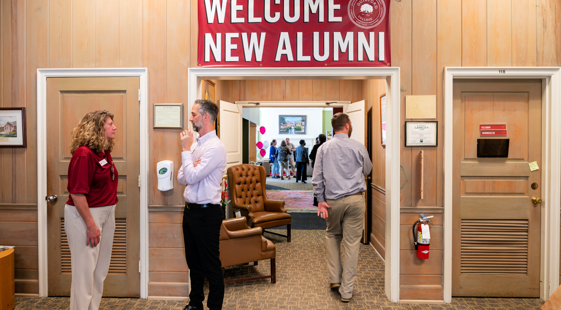 Two Guilford staff stand under a banner that reads, Welcome, New Alumni.