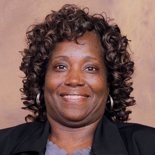 Anastasia Polk-Bethea in a grey shirt and black jacket in front of a mottled brown background