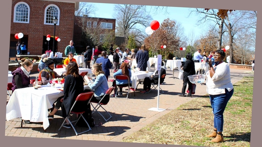 A staff member announces prizes on a microphone while faculty and staff enjoy the outdoor lunch.