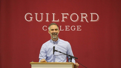 Steve Mencarini in front of hte Guilford College Banner on the stage at Graduation rehearsal 2024
